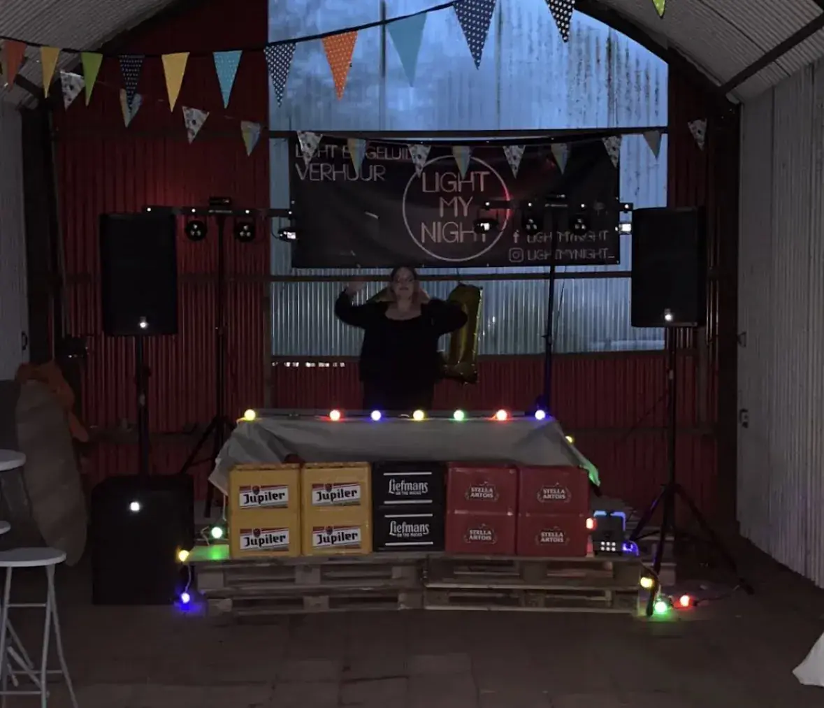 DJ-booth met gehuurde licht- en geluidsset in een loods met paletten